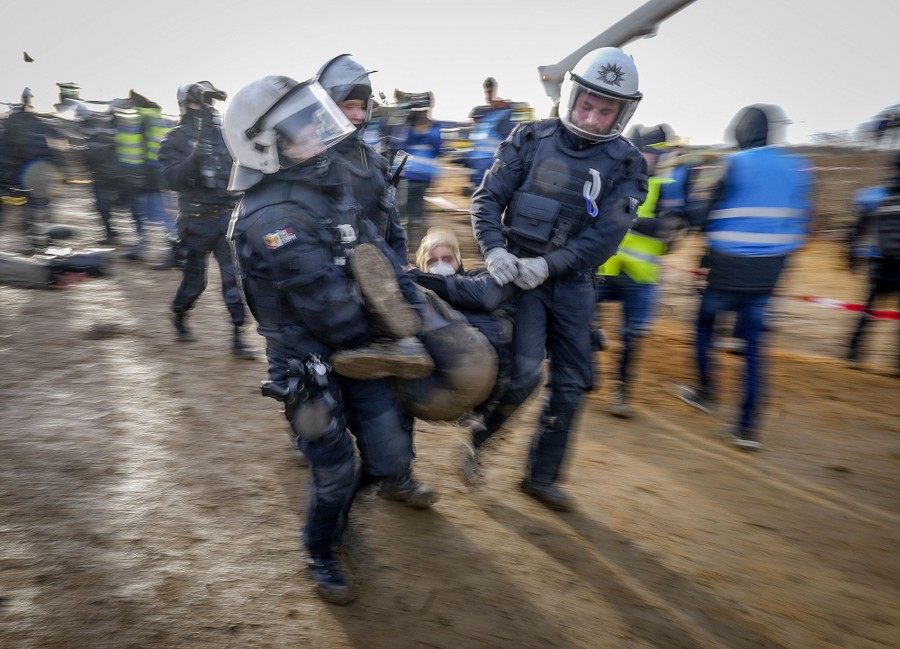 Police officers carry a demonstrator on a muddy road.