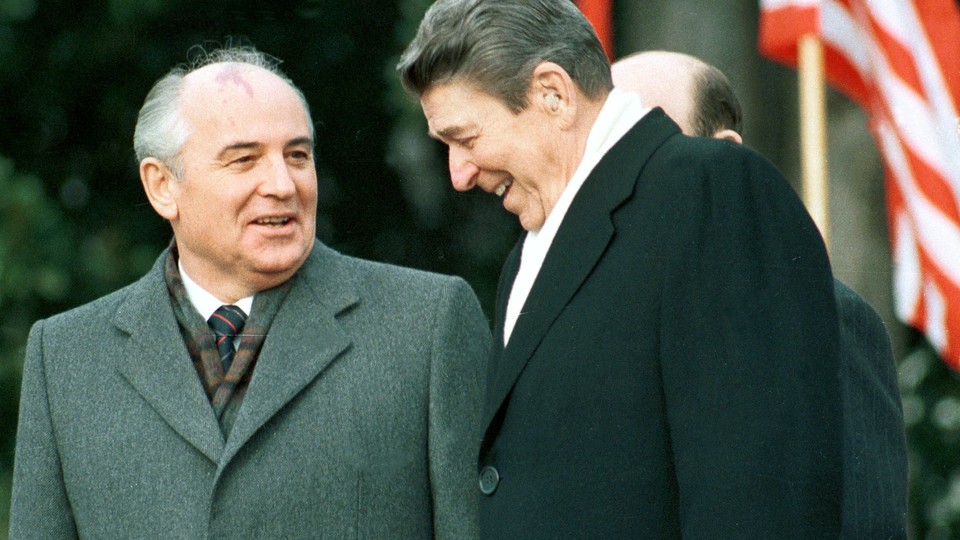 President Ronald Reagan stands with former Soviet leader Mikhail Gorbachev and laugh in front of an American flag.
