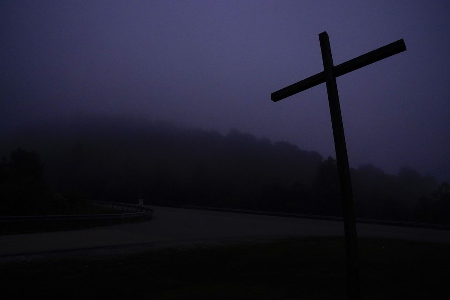 A cross is seen near a hillside under heavy fog.
