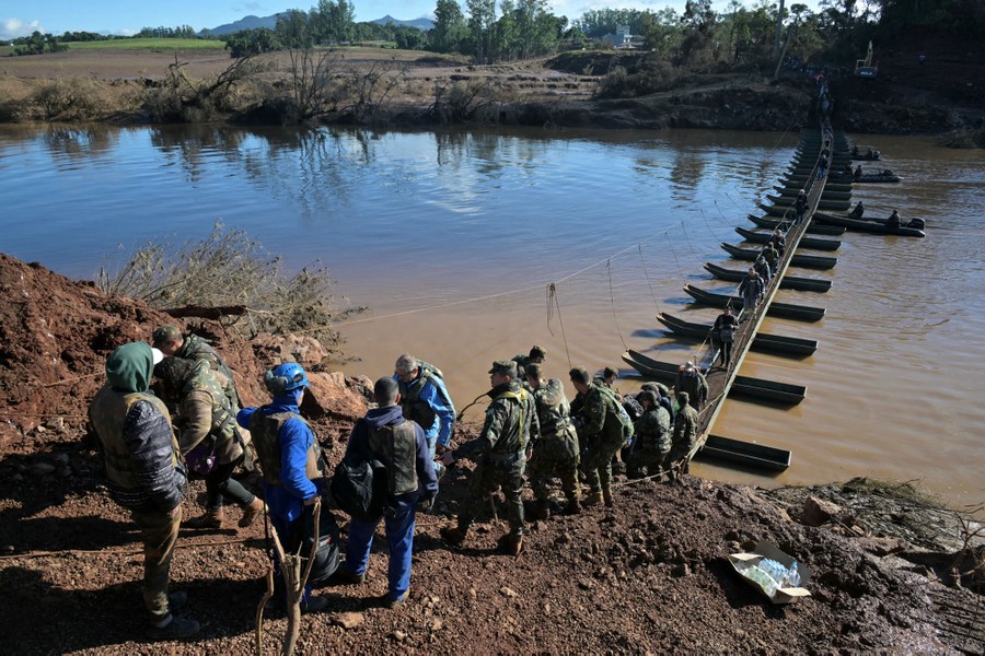 People walk across a temporary floating pedestrian bridge, assisted by soldiers.