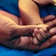 A baby's hand holds an adult's thumb