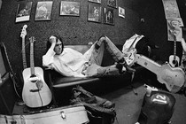 A young Neil Young lying sideways on a couch surrounded by guitars