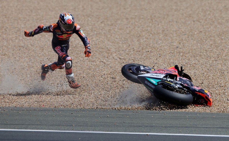 A motorcycle racer chases after their tumbling bike in gravel beside the track, after a fall.