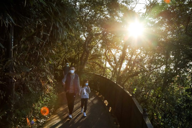 An adult and child in masks walk through a park in Hong Kong