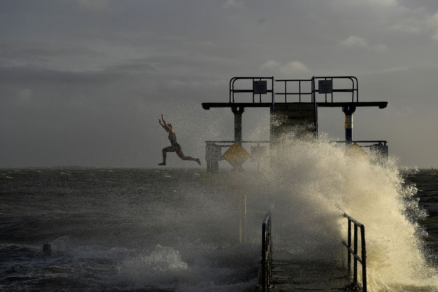 A woman jumps from a diving tower into wind-blown waves.