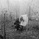 Black-and-white photo of a man trying to protect himself from tear gas among shrubs