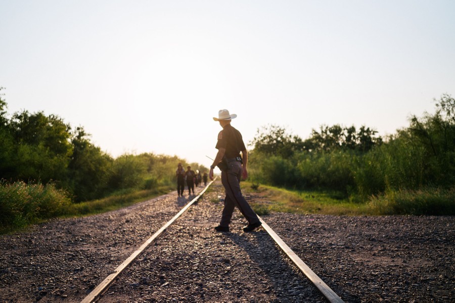 A law enforcement officer walks on railroad tracks to meet migrants as they approach.