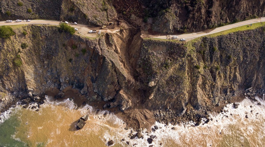 An aerial view of a road with a large section missing amid mud and debris.