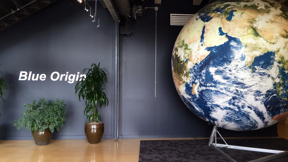 The Washington State office of the spaceflight company Blue Origin is shown, and include a replica of the Earth, some potted plants, and the company's name printed on the blue wall
