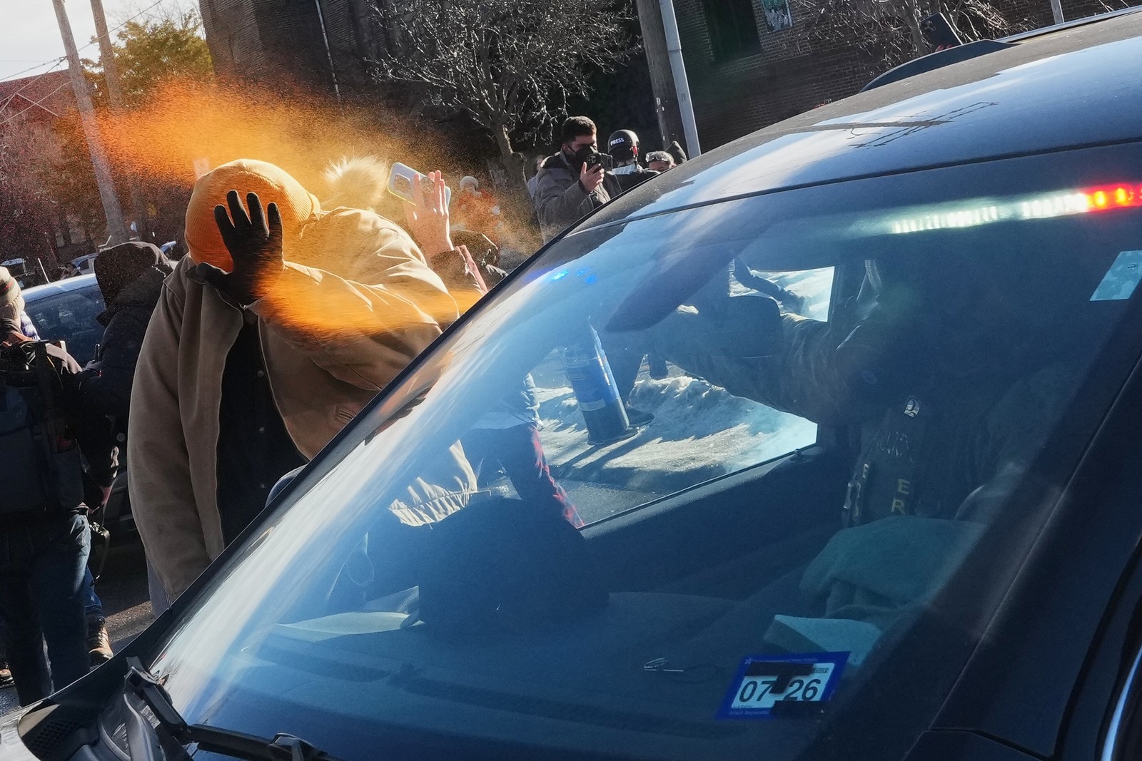 A protester is sprayed with pepper spray by a federal agent who is seated in a car.