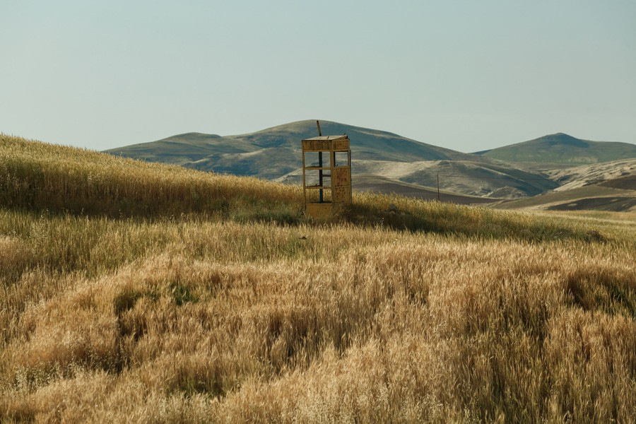 An old phone-booth-size structure stands alone in a field, with empty hills visible in the distance.