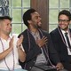 Three men sit with red and white graduation chords. One has his hand over his heart 