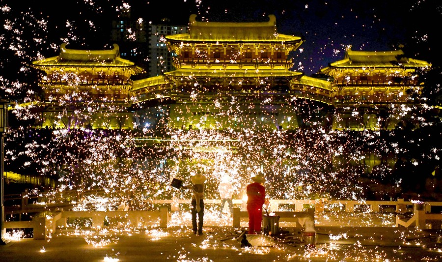 Two performers work together to toss molten iron in the air, creating a cloud of sparks.