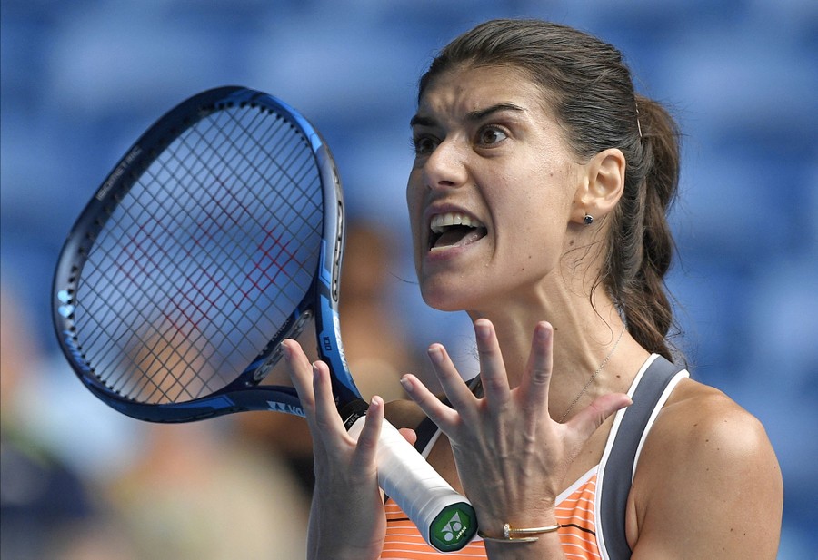 Sorana Cirstea holds her hands and racket up, while animatedly reacting.