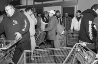 Customers push shopping carts while crowded in a small room.