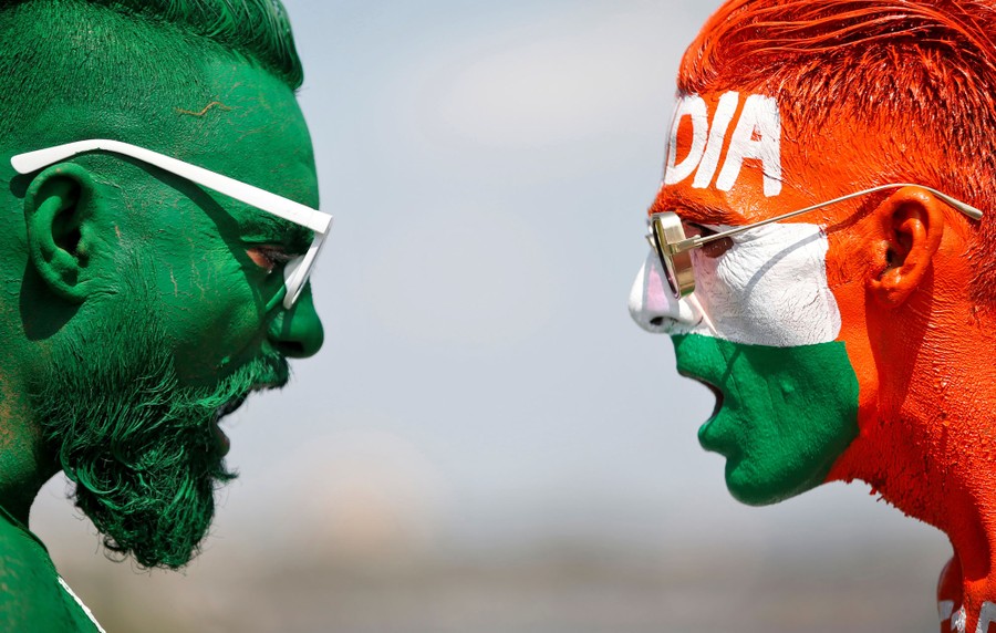 Two cricket fans shout toward each other, with their faces painted in the Indian and Pakistani national-flag colors.