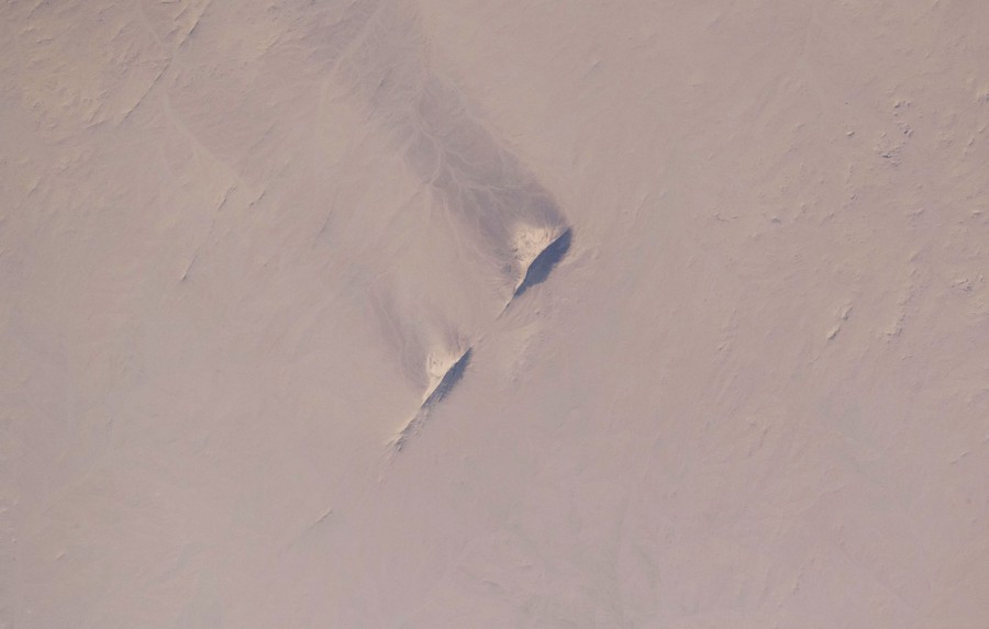An aerial view of windswept hills set in a broad flat desert plain.