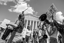 Fotografía en blanco y negro de manifestantes antiaborto tocando tambores y gritando con megáfonos frente a la Corte Suprema, sosteniendo carteles, incluyendo uno que dice, “¡Las PÍLDORAS abortivas son ASESINAS!”.