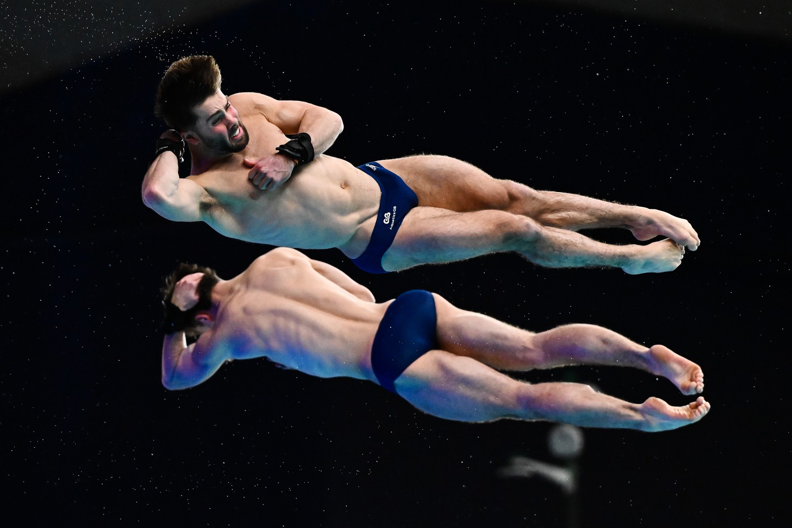 Two divers, seen stretched out in the air, spinning, mid-dive.