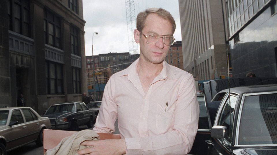 A photograph of Goetz on the way to his trial, wearing a pink button down shirt and glasses.