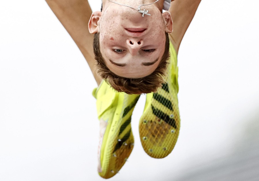 An athlete leaps over a high jump, his face and feet upside down in midair.