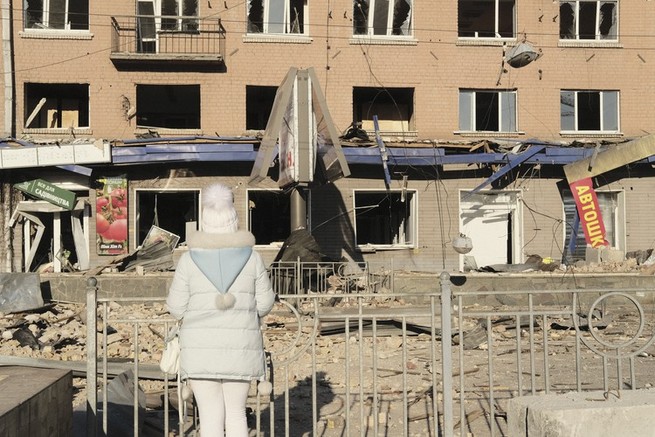 A woman in white stands before a shelled building