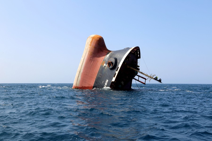 The bow of a partially sunk cargo ship pokes out of the ocean.