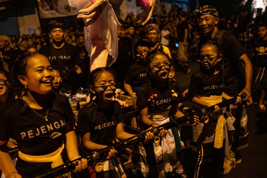 Young people laugh and scream while carrying a sculpture of a demonic creature in a parade.