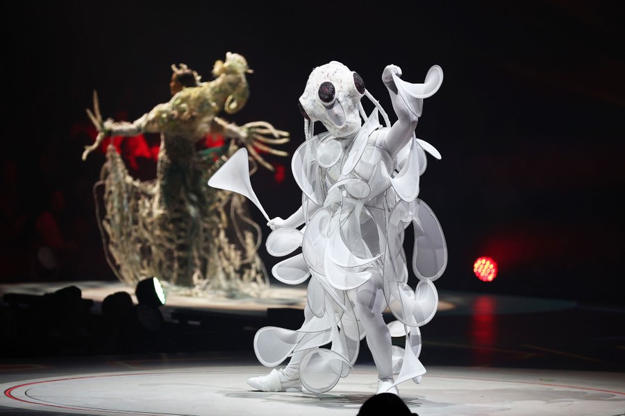 A person poses while wearing a costume covered in multiple curls and swoops of white fabric.