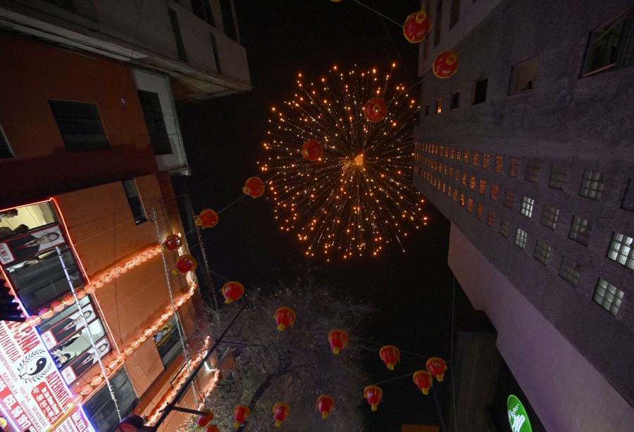 A view looking up, past city buildings, at a burst of fireworks exploding overhead