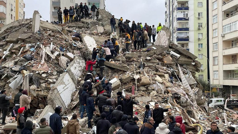Dozens of people stand in a loose line atop the rubble of a collapsed building, passing an injured person down.