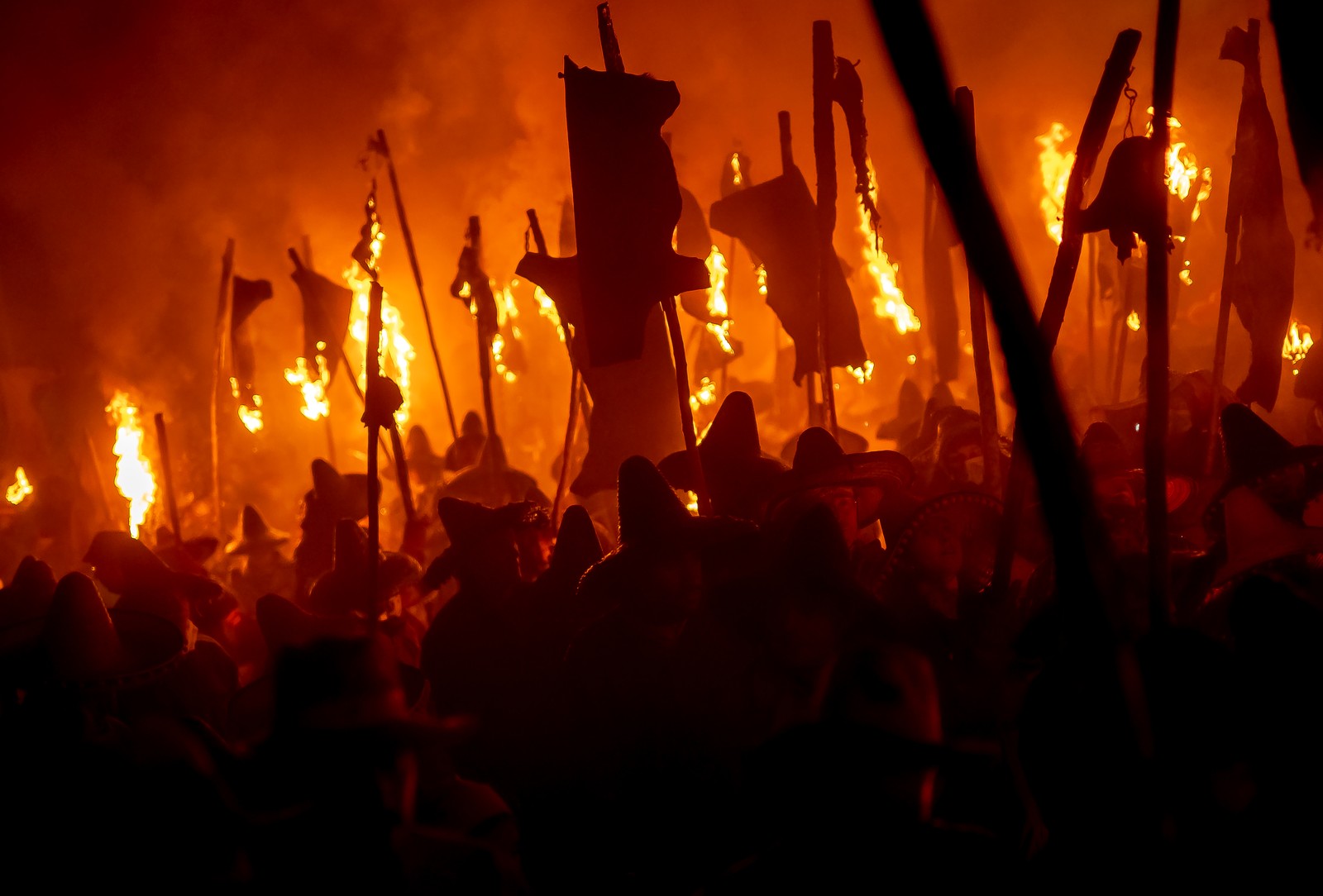 A group of costumed people carrying torches march in a parade procession.