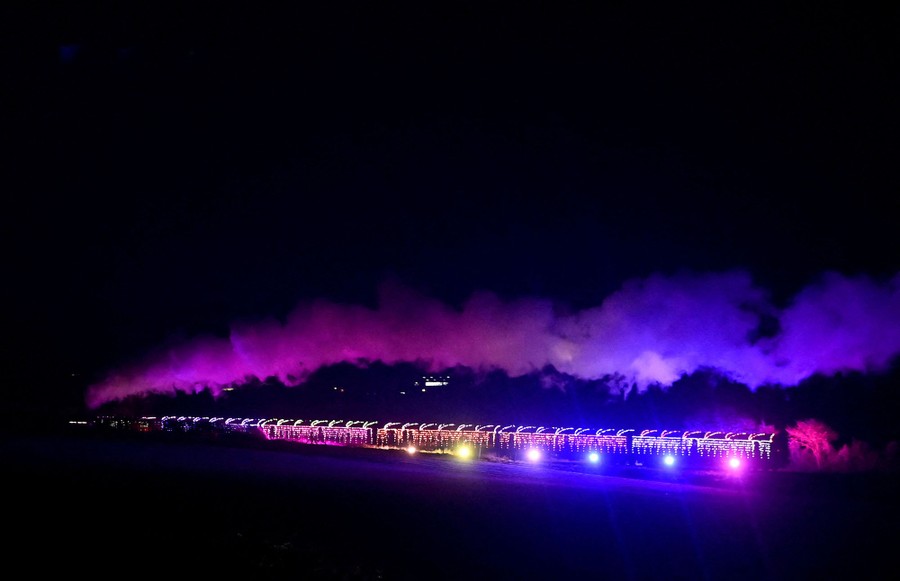 A passenger steam train, decorated with Christmas lights, travels at night.