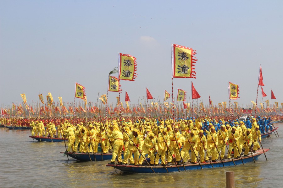 Hàng trăm người trong trang phục đồng phục đứng cùng nhau trên những chiếc thuyền lớn, chèo.