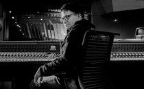 A black-and-white photo of Steve Albini in glasses and a hat, sitting in a recording studio