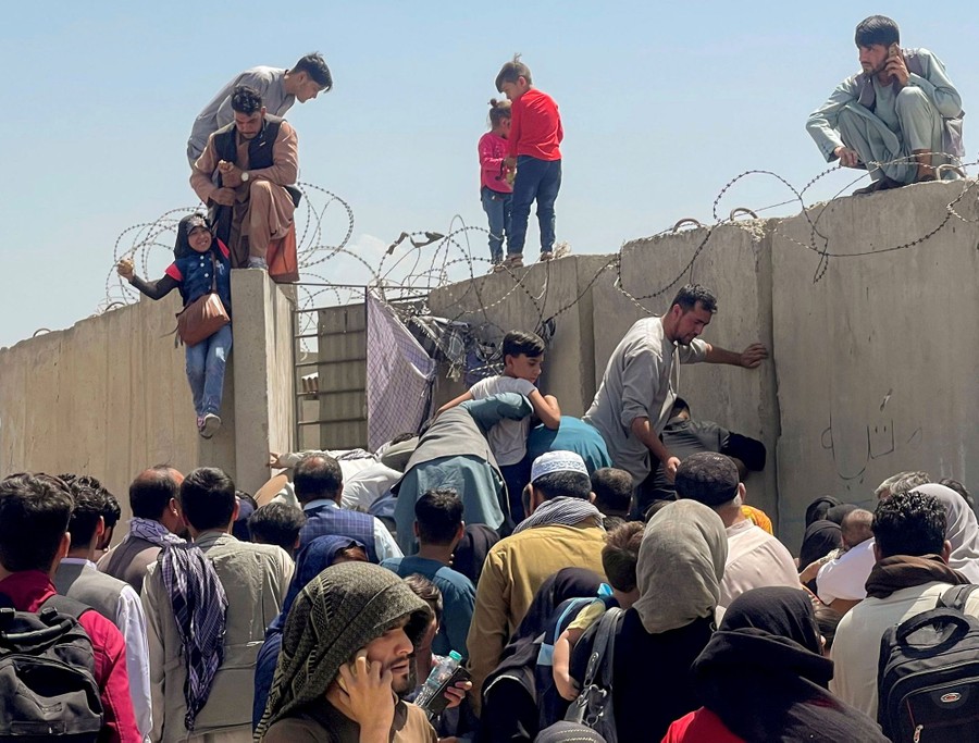 A man pulls a girl up onto the top of a tall concrete wall, among a crowd of people.