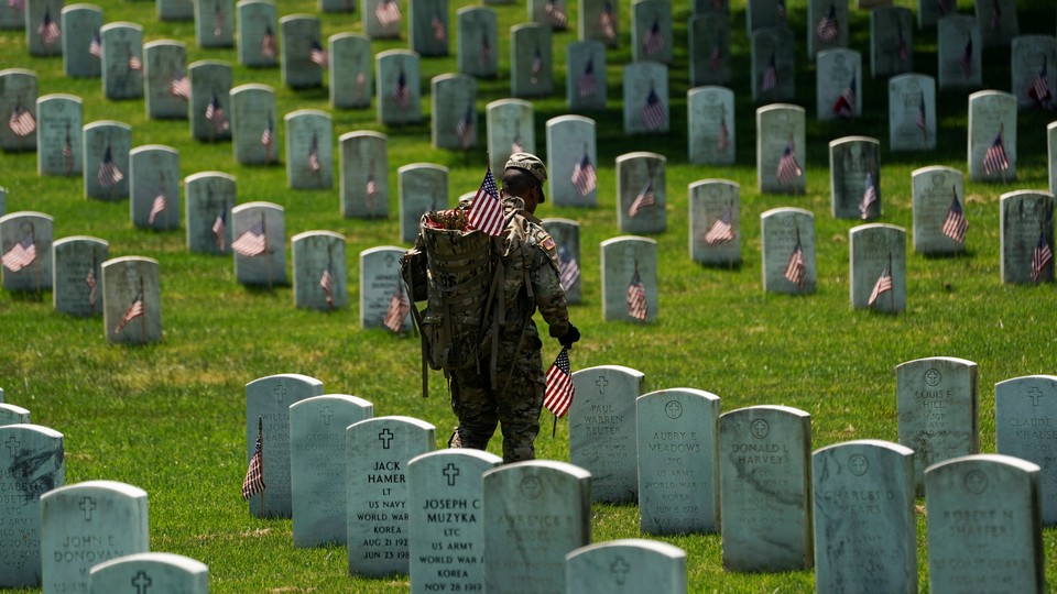 An Old Guard places American flags by headstones in Arlington National Cemetery.