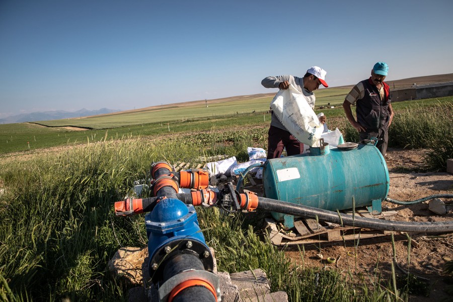 Two men work beside a pump and irrigation rig in a farm field.