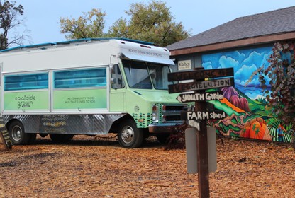 A green and blue food truck parked outside a colorful building