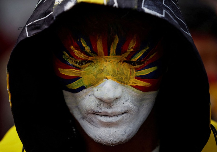 A protester with the flag of Tibet painted on his face looks downward.