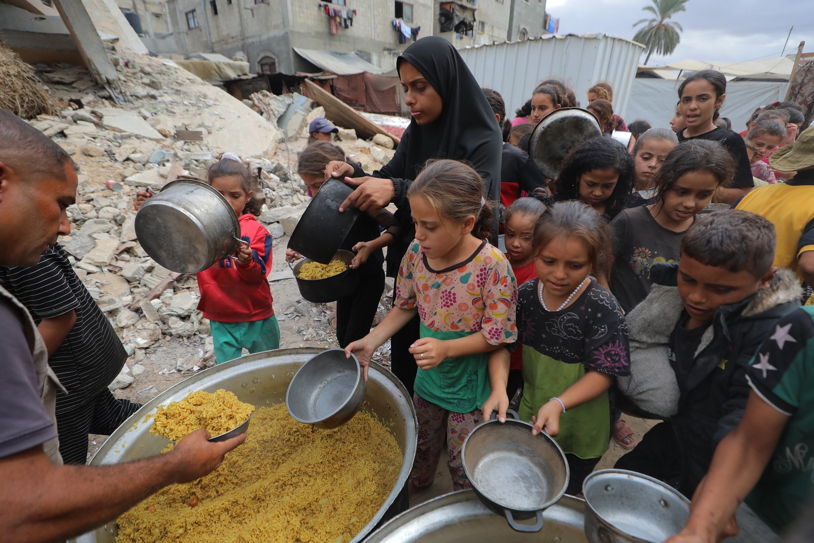 A group mostly made up of children wait for food in Gaza, holding out pots.