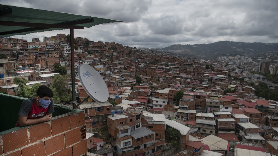 A person wearing a mask looks out over a view of the Petare slum in Caracas, Venezuela.