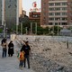 A Iranian family walks by a field of rubble in an urban neighborhood, the young boy carrying an Iranian flag.