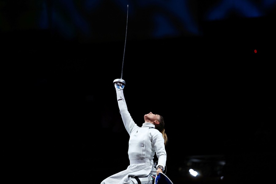 A wheelchair fencer raises her sword in celebration.