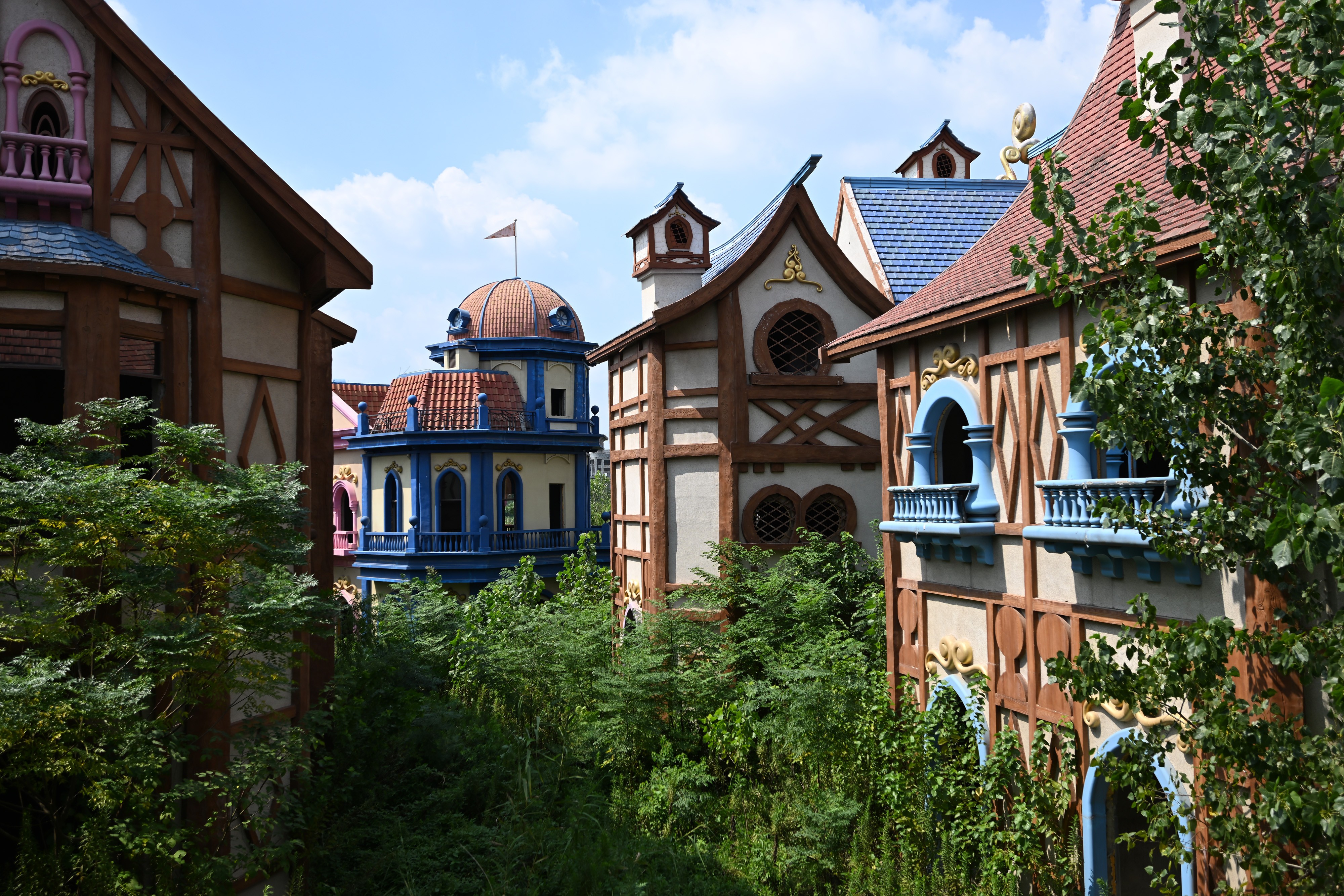 Young trees grow around colorful theme park buildings in an abandoned site.