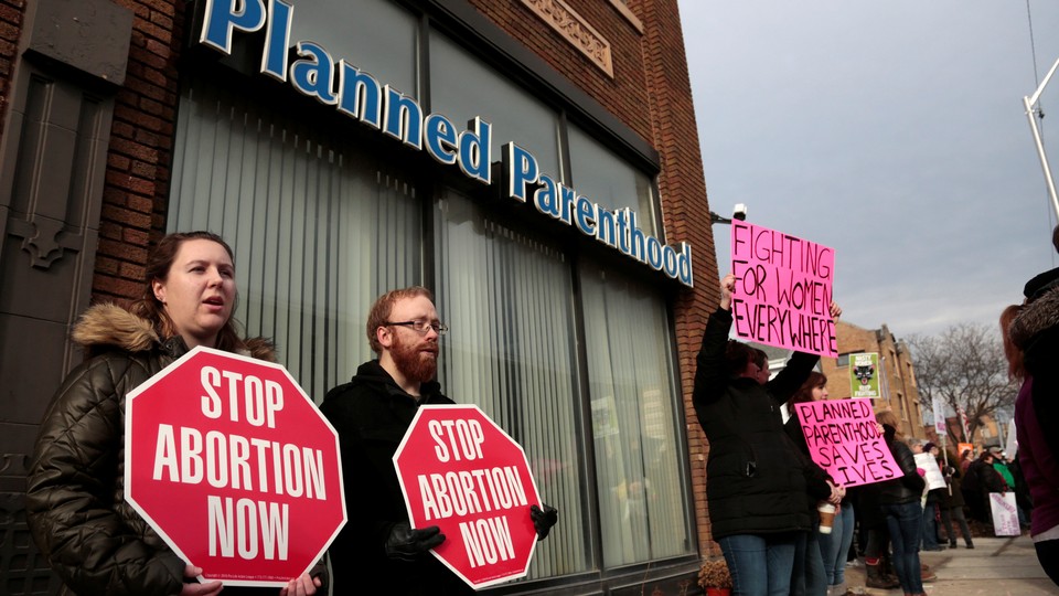 Protsters stand outside a Planned Parenthood clinic holding signs.