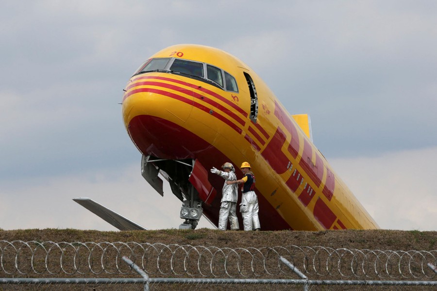 Two emergency workers stand at the front end of an aircraft that crashed on a runway.