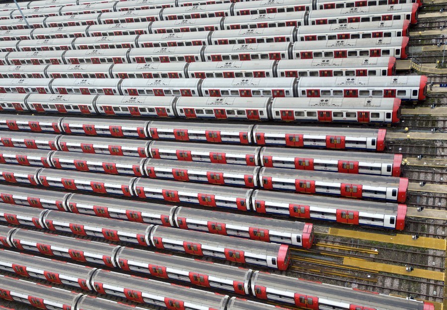 About two dozen subway trains sit side-by-side on rails in a rail yard.
