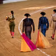 photo of female bullfighter walking in ring looking at crowd, followed by three men with pink and gold capes
