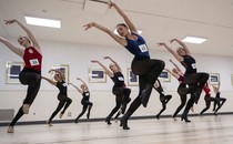 About a dozen dancers perform together in a studio during an audition.